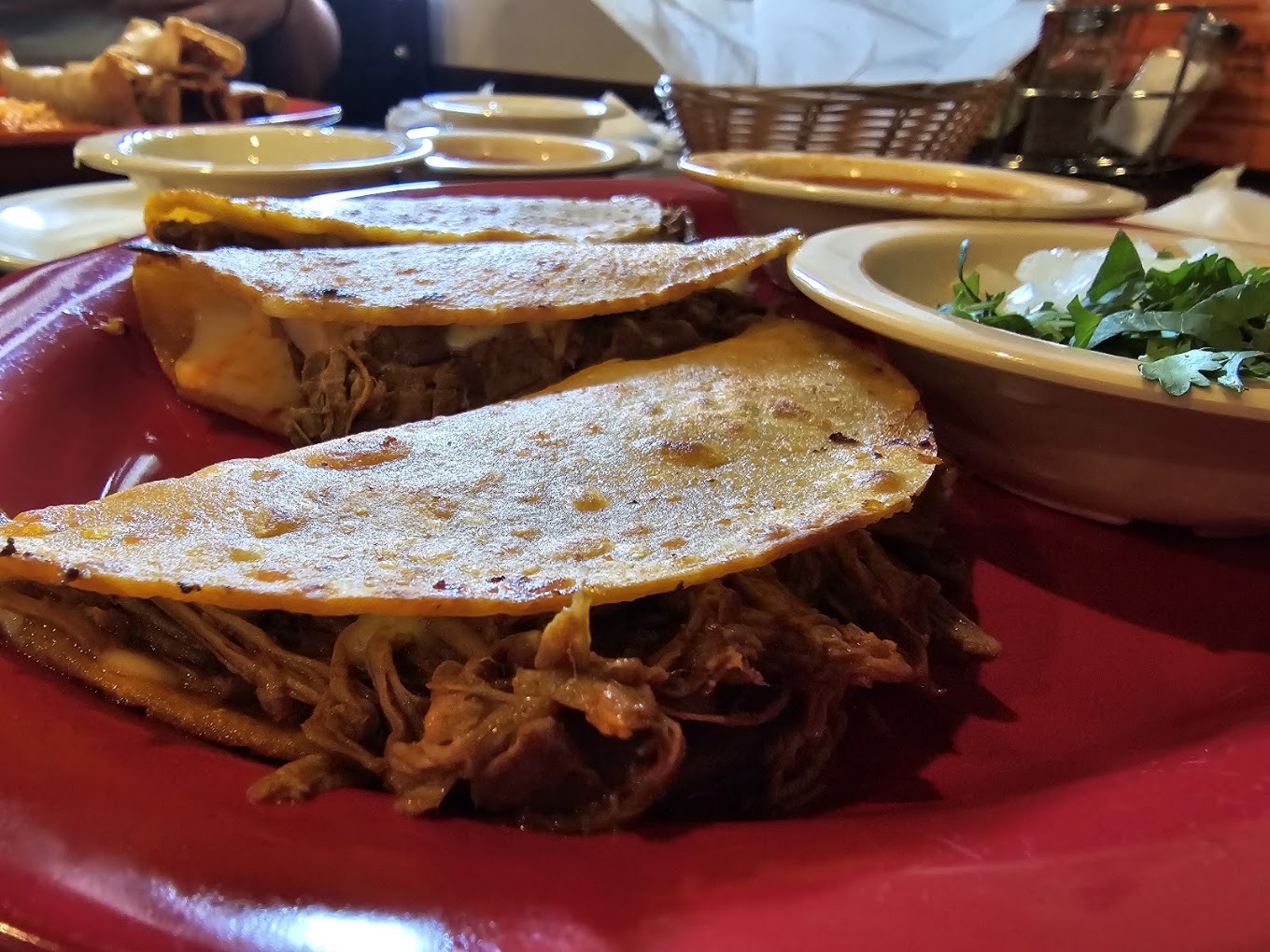 Quesa birria tacos glowing in low light on a deep red plate at the table