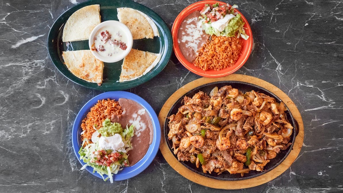 A cast-iron platter heaped with steak, chicken and shrimp fajitas surrounded by combo plates